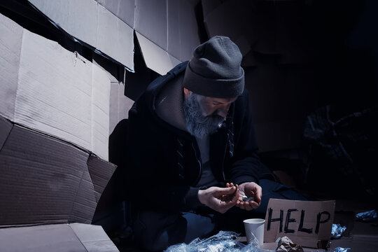A homeless bearded man sits on boxes on the street and asks for help. Need a homeless person asks for money for food and overnight.