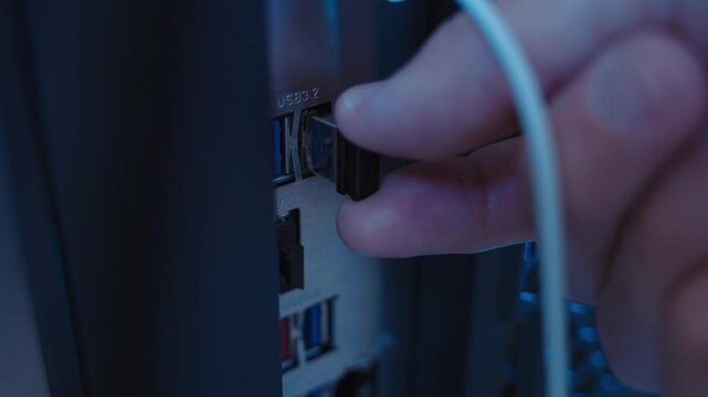 Desktop computer close up as hand inserts small flash drive in dark room. Night in business company or office. Mysterious suspicious activity. Stealing data and information or installing malware app