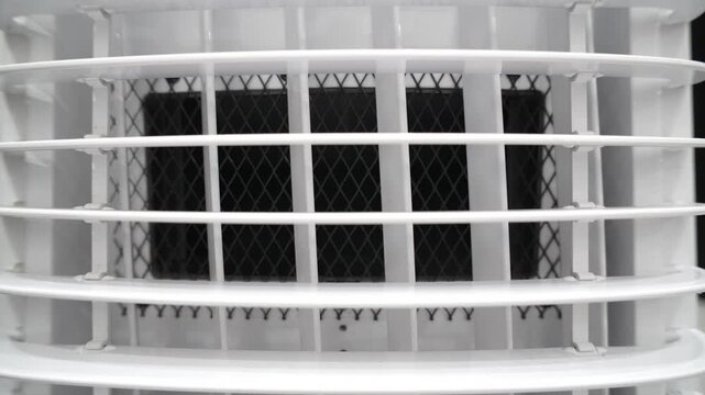 Close-up of white plastic air conditioner or cooler vent with protective black mesh grille. Industrial abstract background of ventilation system.