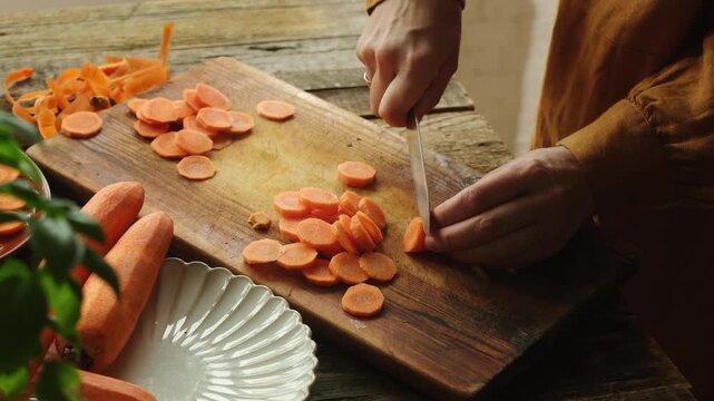 Woman slicing fresh carrot. Cooking process. Preparing healthy vegan or vegetarian meal. Everyday routine. Raw food diet.