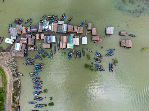 Aerial view of Kalabagi village with traditional thatched houses and numerous blue fishing boats moored in the water, Khulna District, Khulna Division, Bangladesh.