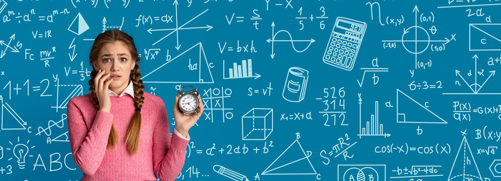 A student stands in front of a chalkboard filled with math equations and shapes. She holds an alarm clock and looks concerned. It looks like she is preparing for a test under time pressure.