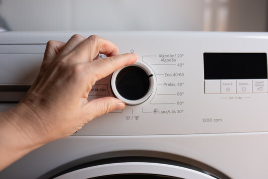 A hand adjusts the circular program selection knob on a white washing machine with Russian text.