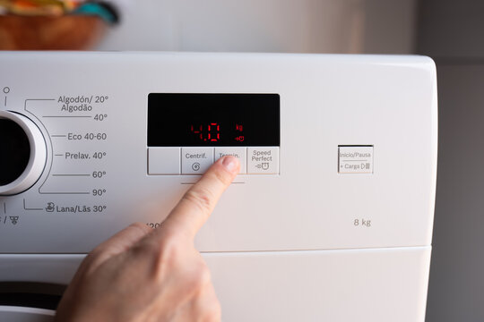 Close up hand pressing button on white washing machine with digital red display four kilograms