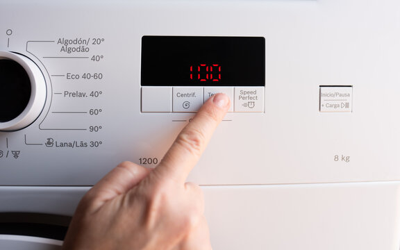 Finger pressing button on washing machine control panel showing value one thousand one hundred electronic