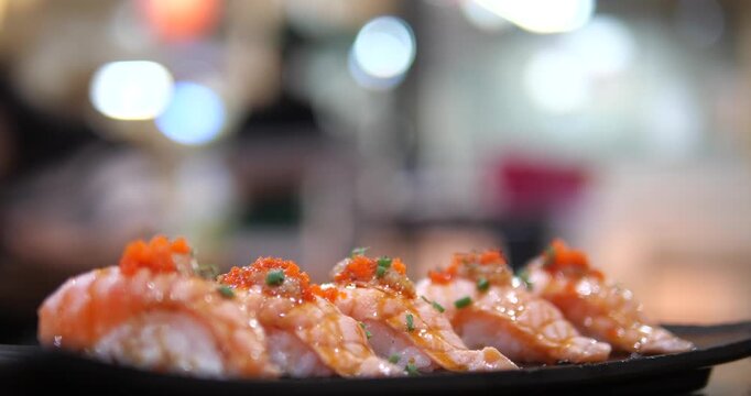 Cinematic close-up of Aburi salmon sushi topped with Ebiko (shrimp roe) on a black tray, fresh Japanese cuisine with beautiful bokeh background