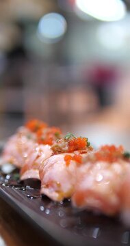Cinematic close-up of Aburi salmon sushi topped with Ebiko (shrimp roe) on a black tray, fresh Japanese cuisine with beautiful bokeh background