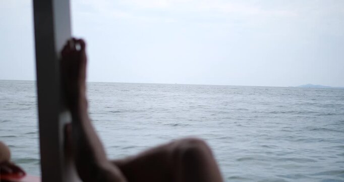 Cinematic wide view of a traveler relaxing on a boat, silhouette of feet resting while looking at the vast ocean, vacation and freedom concept