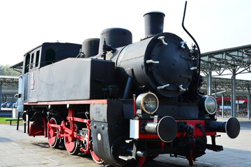 A black historic steam locomotive with red wheels on the platform of an open-air railway museum © Wolf Steppe