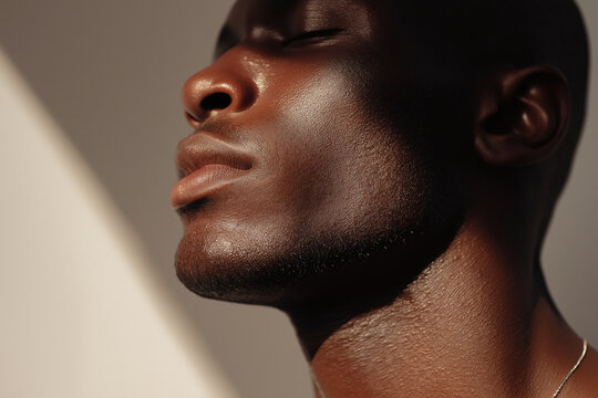 Glossy dark male skin with subtle sweat glow under soft light, close up side profile showing jawline, cheek, nose and neck with warm tones and smooth texture