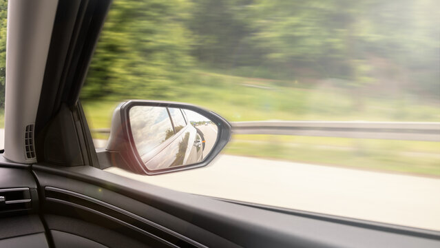 View from moving car with side mirror reflection on highway, motion blur traffic and transportation concept, safety and traffic rules, car insurance, copy-space.