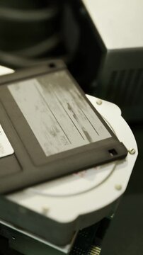 Two old computer parts are placed on a black table. One part is a disk cartridge on top of a round fan like object. There is also a metallic surface in the background.