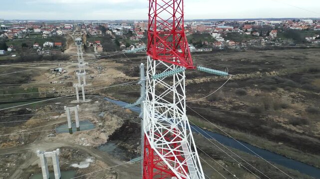 Detailed circular shot of insulators and steel framework at the summit of a power tower, drone video.