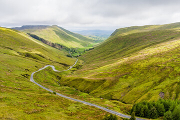 Naklejka premium Aerial view of Glengesh Pass curving through a broad green valley in County Donegal, Ireland. A dramatic birds eye landscape of remote mountains and winding roads