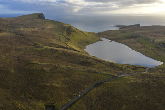 Aerial view of Loch Mor surrounded by rugged green hills and a winding road near the coastline Isle of Skye, Scotland, United Kingdom.