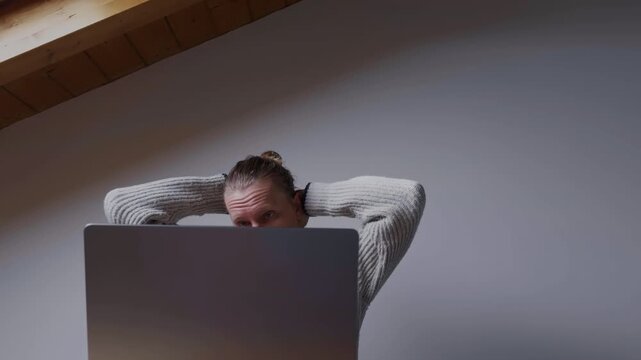 Focused man solving problem while working on laptop at home
Back view of concentrated man looking at laptop screen during remote work session. Stressful business and productivity moment.
