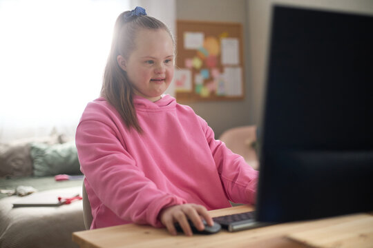 Caucasian child girl with Down syndrome using desktop computer at home, learning and navigating digital content. Supporting inclusive education, accessibility, child development campaigns