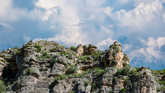 Formaci&oacute;n rocosa caliza t&iacute;pica de zonas monta&ntilde;osas mediterr&aacute;neas. La textura rugosa de la piedra contrasta con el cielo, lleno de nubes densas y luminosas que aportan dramatismo al paisaje.