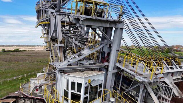 Drone video showing a bucket wheel excavator from bottom to top, featuring the massive steel industrial structure, operator's cabin, heavy crawler tracks, and mechanical details of the boom against th