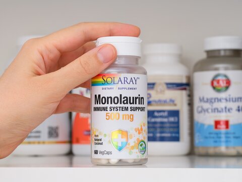 Tambov, Russian Federation - February 19, 2022 Woman taking a bottle of Solaray Monolaurin dietary supplement capsules out of shelf with other supplement jars. Close-up