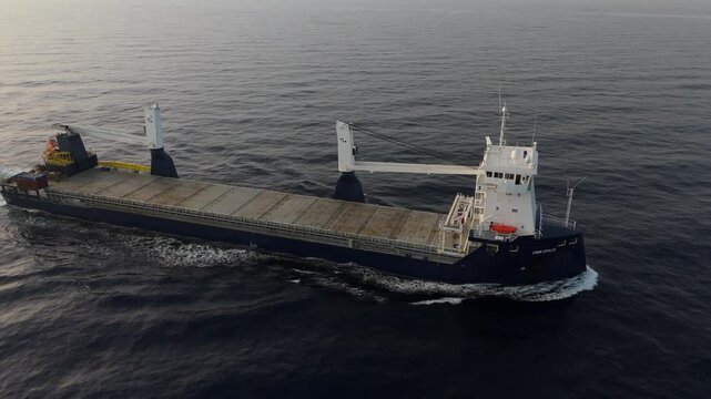 4K drone footage following a heavy-lift vessel from the side, showing the hull and cranes in detail.