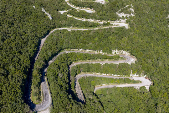 Drone shot of steep serpentine asphalt road zig-zagging through dense mountain forest in Sokraki, Corfu, Greece