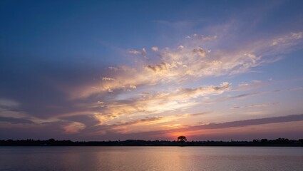 Fototapeta premium Sunset glow over wide lake with silhouetted tree on horizon
