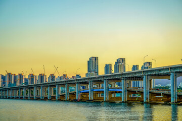 Fototapeta premium Han River Expressway Bridge at Warm Sunset with Active Construction Cranes and Modern Apartment Buildings Rising Behind, Seoul South Korea