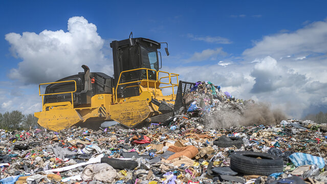 Heavy industrial machinery working at a large landfill site.  A view on a landfill compactor compacting and managing piles of waste.