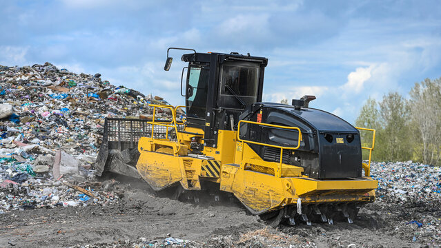 Heavy industrial machinery working at a large landfill site.  A view on a landfill compactor compacting and managing piles of waste.