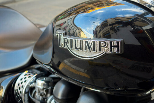Black Triumph motorbike tank showing metallic logo and reflected city buildings.