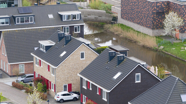 Aerial view of modern residential houses with dark tiled roofs and a small canal in Almere, Flevoland, Netherlands.