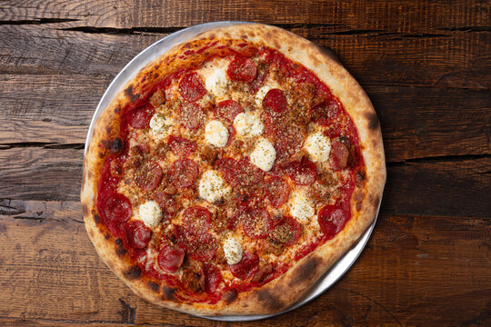 Overhead view of pepperoni and sausage pizza with melted mozzarella and crispy artisan crust on rustic wooden table
