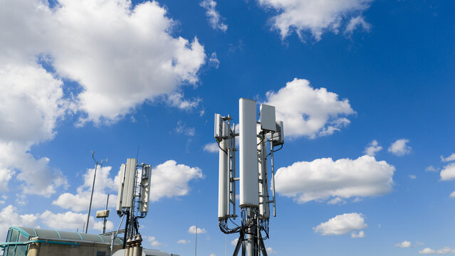 Aerial view of telecommunication antennas and wireless communication equipment on a rooftop under a blue cloudy sky in Amsterdam, North Holland, Netherlands.