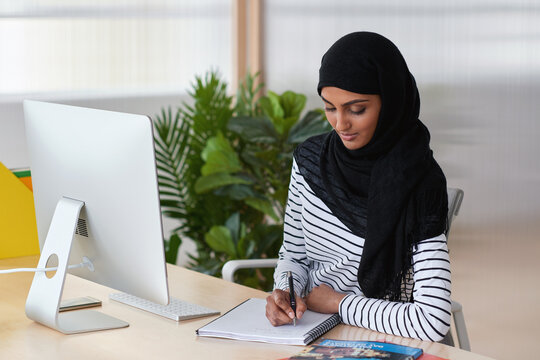 Muslim woman, smile and writing in book at office with checklist, tech or schedule at travel agency. Person with hijab, notes and review with itinerary, location and booking info at tourism company