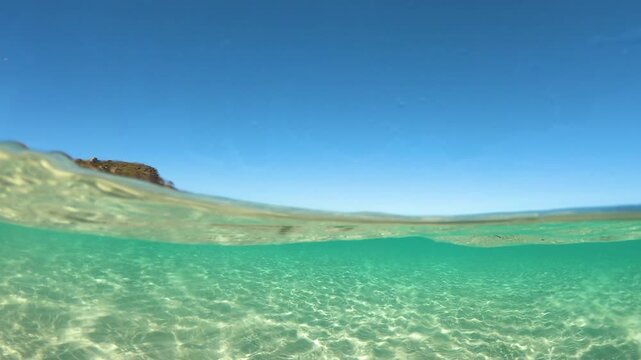 Slow motion split underwater view of crystal clear turquoise sea at La Pelosa Sardinia with distant watchtower and Mediterranean light