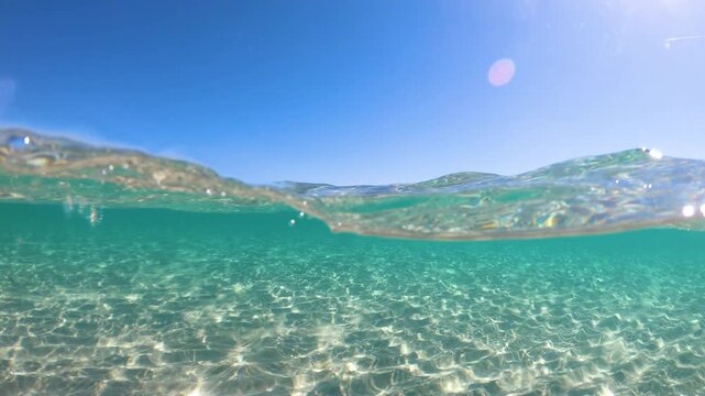 Slow motion split underwater view of crystal clear turquoise sea at La Pelosa Sardinia with gentle surface movement and Mediterranean light