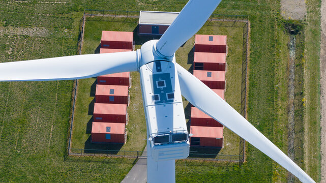 Aerial view of a wind turbine nacelle and blades above red shipping containers in a fenced enclosure Middelharnis, South Holland, Netherlands.