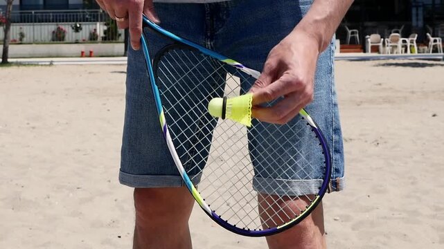 Close-up of speed badminton racket and shuttlecock in hand, outdoor summer crossminton game on sandy beach, fast-paced sport, active lifestyle, fitness, fun and recreational activity.