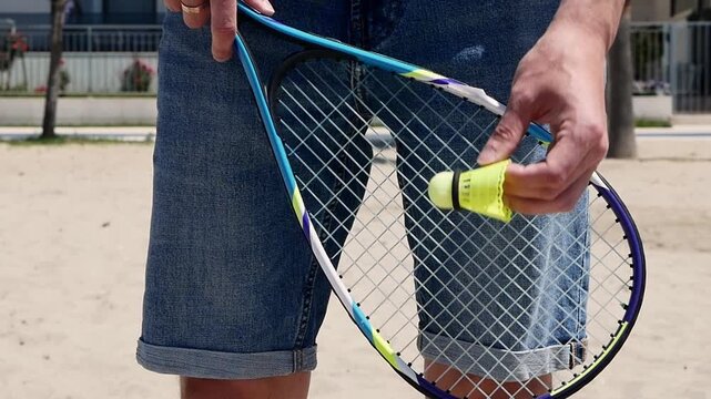 Close-up of speed badminton racket and shuttlecock in hand, practicing serve on sandy beach, outdoor crossminton game, fast-paced summer sport, active lifestyle .