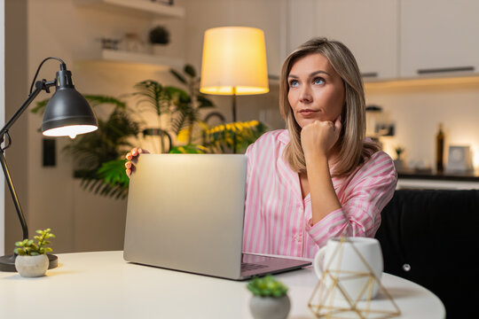 Adult woman at night home works on laptop feels tired powers off device closes lid to rest. Caucasian girl on sofa at evening at table on sofa decides to continue tomorrow plans tasks notes new start.