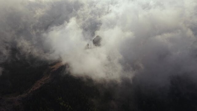 Epic aerial view of the Roque Nublo volcanic rock monolith appearing through moving clouds and mist in the mountains of Gran Canaria