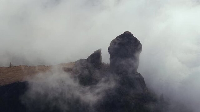 Misty clouds swirling and moving around the iconic Roque Nublo volcanic rock formation. Dramatic and moody landscape in Gran Canaria, Canary Islands