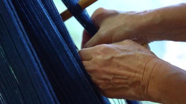 Close up of hands weaving dark blue threads on traditional loom