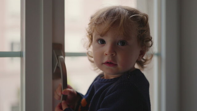 Toddler raising hand toward camera as if saying stop while standing by window showing strong expression playful assertiveness and emotional reaction