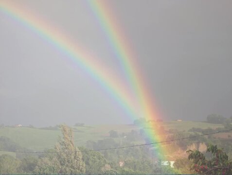 Arcobaleno su paesaggio rurale con campi verdi e cielo nuvoloso, ripresa naturale ideale per contenuti meteo, documentari e fenomeni ottici
