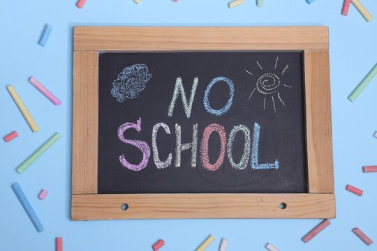 Small chalkboard with words No School, drawings and pieces of chalks on light blue background, flat lay