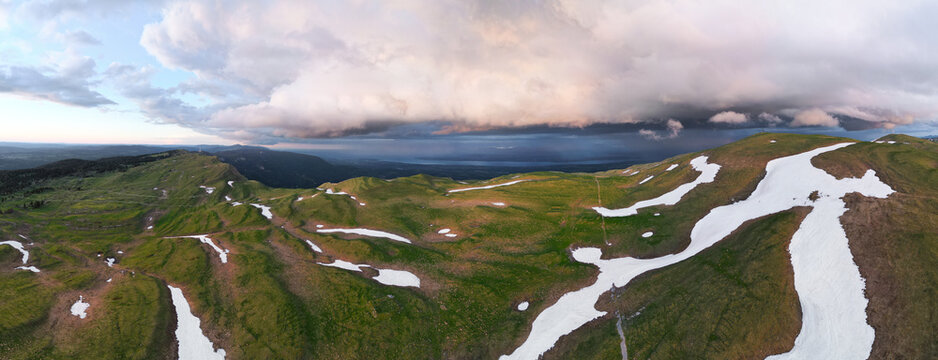 Aerial view of Le Colomby de Gex mountain ridge with patches of snow and dramatic storm clouds over the valley in Echenevex, Auvergne-Rhone-Alpes, France.