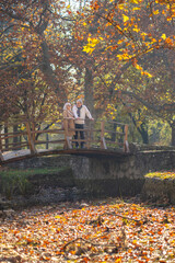 Obraz premium Senior couple enjoying a peaceful autumn day on a wooden bridge in the park