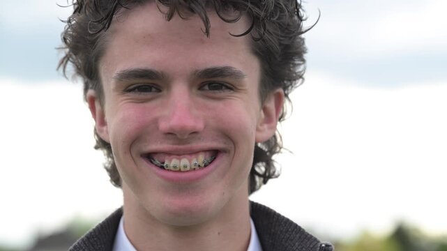 Close-up portrait of smiling young man with braces looking at camera outdoors in soft natural light. Happy male showing healthy teeth and confident smile.


